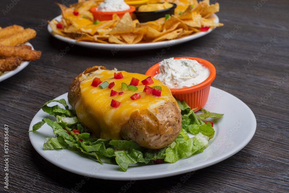 Baked potatoes with cheese topping and dip on a wooden table Baked potatoes with cheese topping and dip on a wooden table