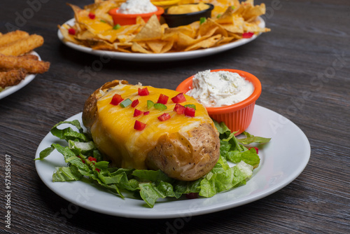 Baked potatoes with cheese topping and dip on a wooden table 