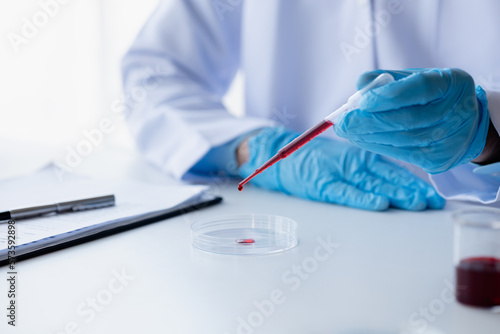 Lab assistant  a medical scientist  a chemistry researcher holds a glass tube through the blood sample  does a chemical experiment and examines a patient s blood sample. Medicine and research concept.