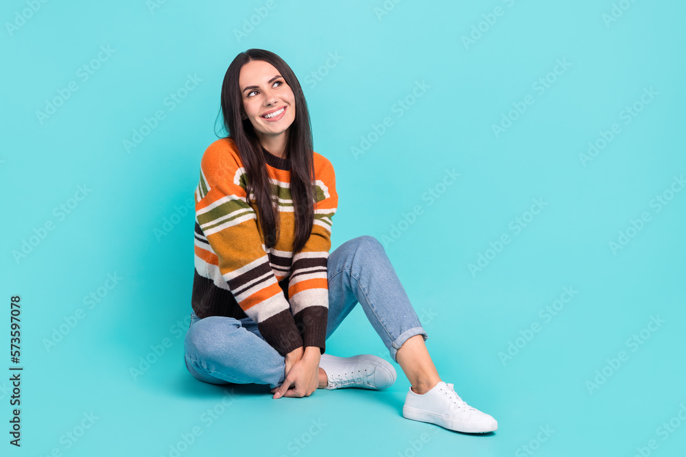 Full length photo of dreamy cute woman wear striped sweater looking empty space sitting floor isolated turquoise color background Full length photo of dreamy cute woman wear striped sweater looking empty space sitting floor isolated turquoise color background