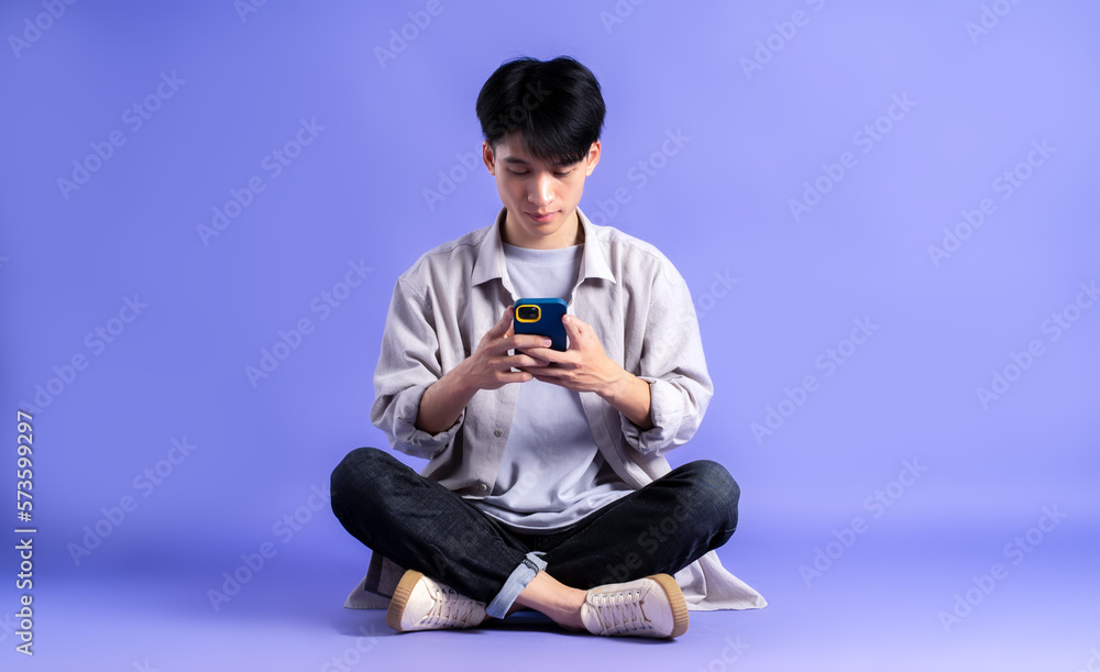 full body image of young asian man using phone on purple background full body image of young asian man using phone on purple background