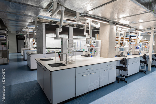 Chemistry lab with white cabinets, chemist workstations and swivel castor chairs. High room. Chemical preparations, test tubes and chemical devices.