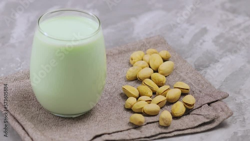 Pistachio milk in glass with pistachionuts on gray background. Vegan plant based milk. Tilt up photo