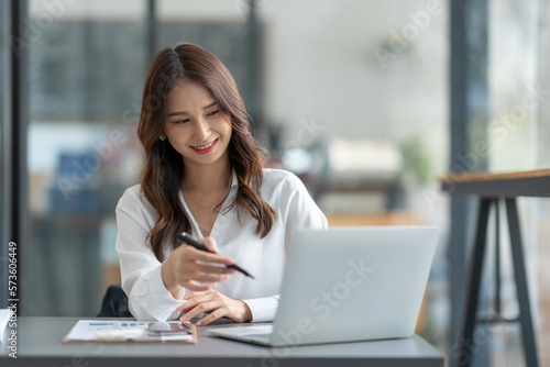 Asian businesswoman using a laptop to communicate Discuss and detail information about jobs online. Finance, accounting, income, and smiling happily at work.