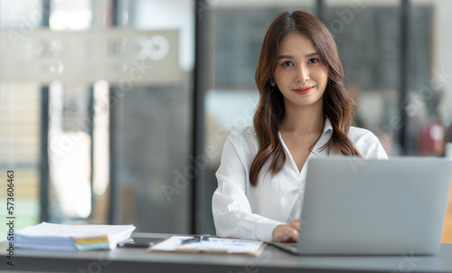 Asian businesswoman using a laptop to communicate Discuss and detail information about jobs online. Finance, accounting, income, and smiling happily at work.