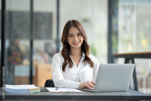 Asian businesswoman using a laptop to communicate Discuss and detail information about jobs online. Finance, accounting, income, and smiling happily at work.