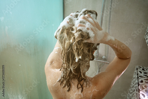 Back view of naked woman taking shower in shower stall. Woman washing her hairs in bathroom. Morning hygiene