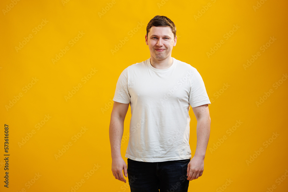 Young handsome man wearing white t-shirt with happy face smiling and looking at the camera over yellow studio background. Positive person Young handsome man wearing white t-shirt with happy face smiling and looking at the camera over yellow studio background. Positive person