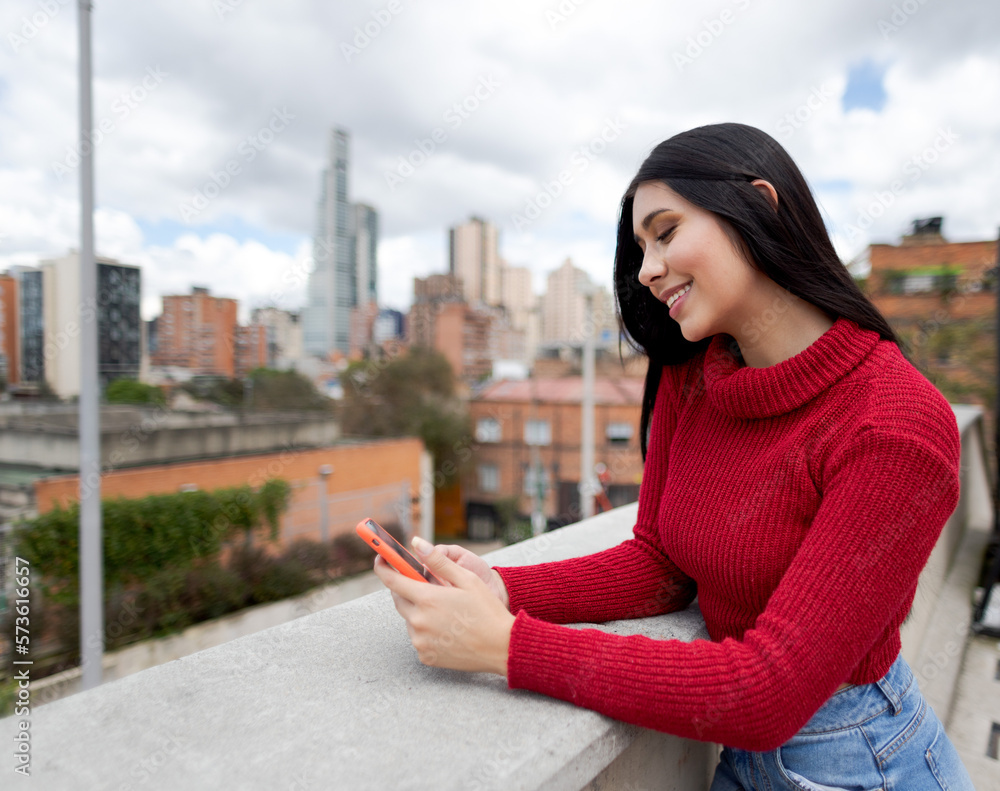 Fototapeta premium smiling woman using smartphone. Girl with black hair and red jacket smiles using smartphone.