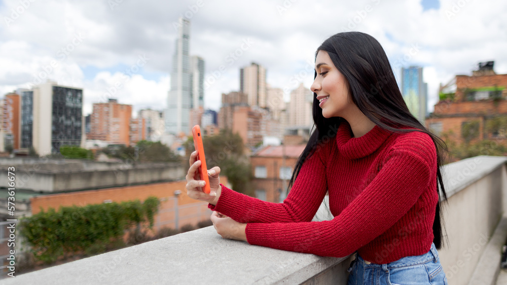 smiling woman using smartphone. Girl with black hair and red jacket smiles using smartphone.