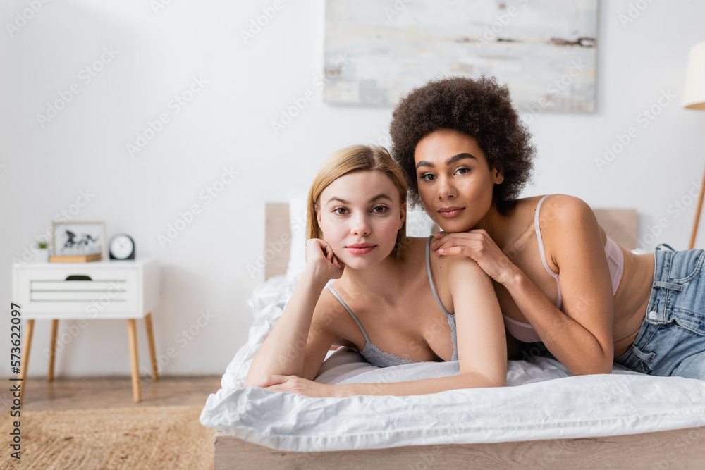young and pretty interracial women looking at camera while lying on bed at home. young and pretty interracial women looking at camera while lying on bed at home.