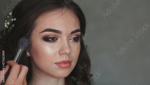 Girl make-up artist applies powder on the face of the model.