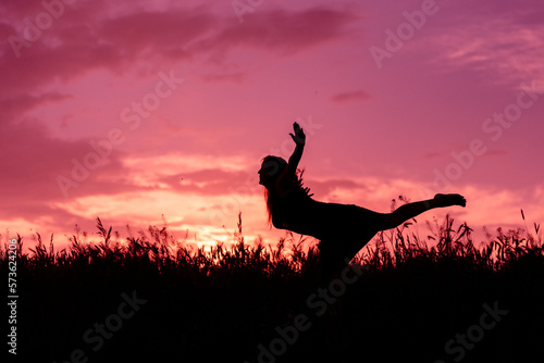 The silhouette of a trip girl over the grass on the background of a pink sunset © Iuliia