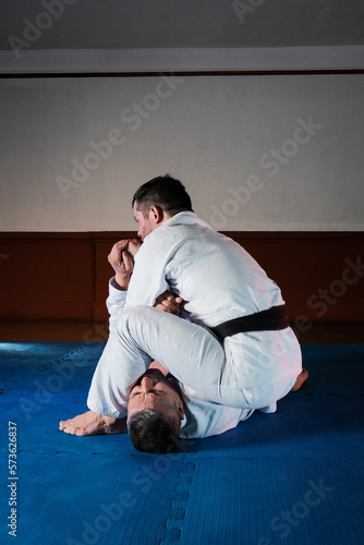 Two latin men training martial arts with kimonos and one black belt and one white belt. the teacher showing step by step how to develop a well done technique.