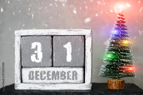 Photography December 31 on wooden calendar background of Christmas tree with garlands and falling snow