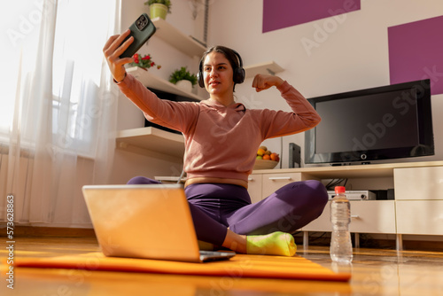Teen girl  takes a selfie while doing sport exercise at home, watching tutorials on a laptop. How to keep fit indoors