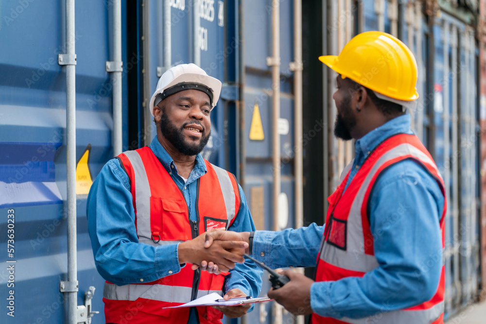 Portrait of Two African Engineer or foreman wears PPE shaking hand with cargo container background at sunset. Logistics global import or export shipping industrial concept. Portrait of Two African Engineer or foreman wears PPE shaking hand with cargo container background at sunset. Logistics global import or export shipping industrial concept.