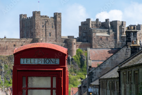 Close up of a traditional red UK telephone box in the village green at Bamburgh  UK  against out of focus castle
