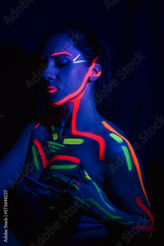 Fashion model woman in neon light, portrait of a beautiful model with fluorescent makeup, body art design in UV, painted face, colorful makeup, on a black background of a girl. 