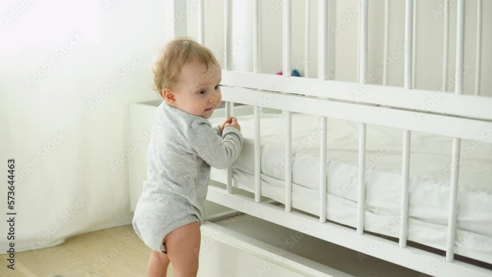 Baby taking first steps near the bed. Little girl learning to walk Baby taking first steps near the bed. Little girl learning to walk