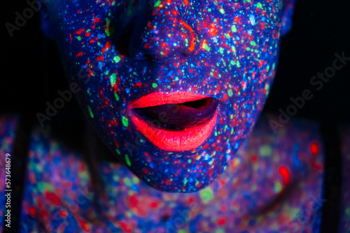Fashion model woman in neon light, portrait of a beautiful model with fluorescent makeup, body art design in UV, painted face, colorful makeup, on a black background of a girl. 