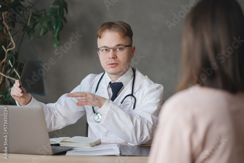 male doctor communicates with female patient in office, examines X-ray picture. in clinic male traumatologist is at reception, a virologist, immunologist, endocrinologist prescribes treatment drugs