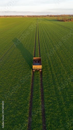 Hänger von einem Traktor steht auf einem grünen Feld mit Spuren, Symmetrisch von oben hochkant