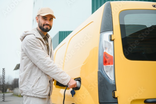 Man Holding Power Charging Cable For Electric Car In Outdoor Car Park. And he s going to connect the car to the charging station in the parking lot near the shopping center