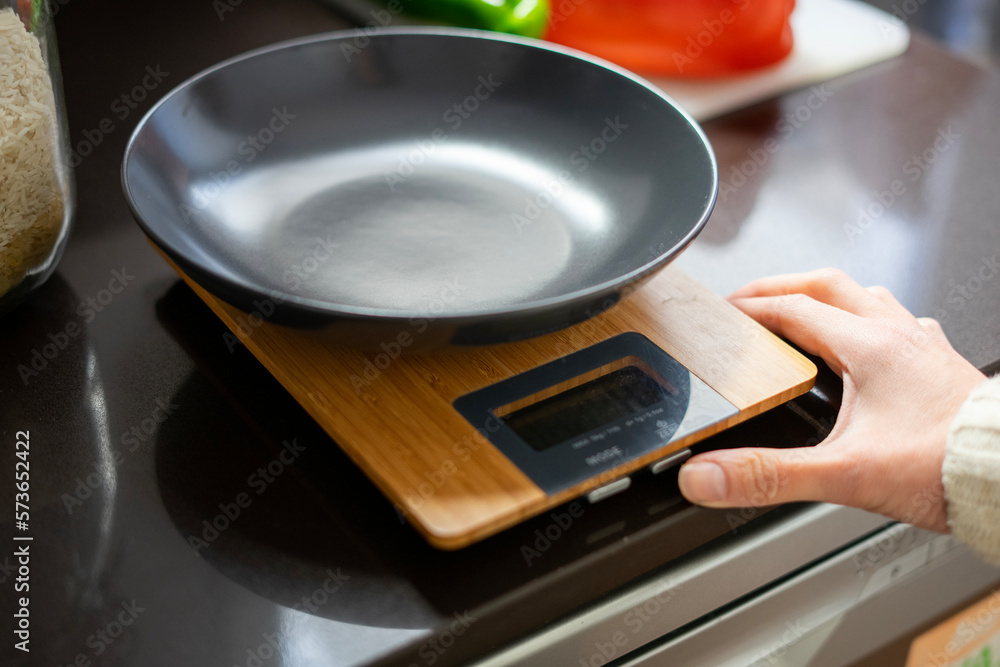 Girl cooking. Girl turning on the kitchen scale, to weigh the rice