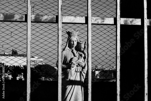 Statue of Madonna with child behind an iron gate, in the background panorama of the Appio district of Rome. photo