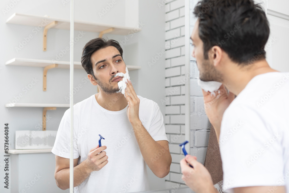 Handsome man looking at the mirror and shaving in the bathroom Handsome man looking at the mirror and shaving in the bathroom