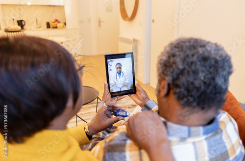 African American senior couple talk to their doctor over video call from home