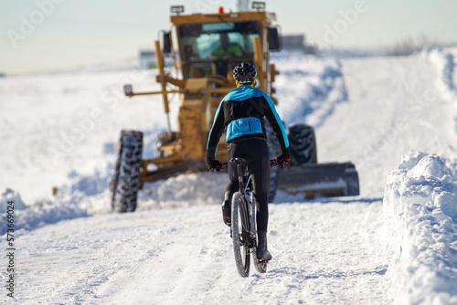 cyclist facing snow plow clearing a road in winter