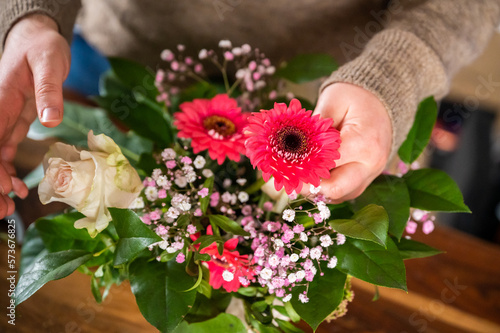 Female florist is putting beautiful spring flowers together in a vase indoors  no visible face