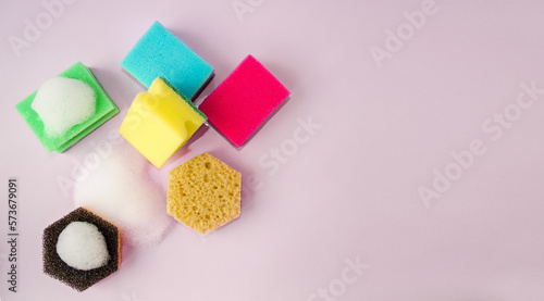 On a pink background, multi-colored sponges for washing dishes and cleaning the house.  Copy space for text, flat lay, background graphic, top view.  The concept of cleanliness in the house.