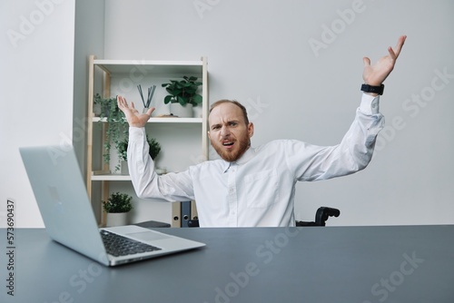 A man in a wheelchair businessman with tattoos in the office behind a laptop, anger and annoyance, hands up, the concept of working a person with disabilities, freedom from social frames
