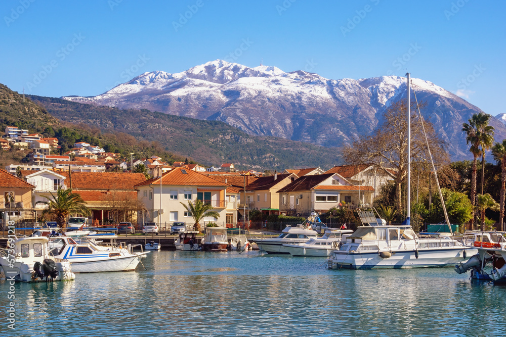 Beautiful winter Mediterranean landscape. Montenegro, Tivat city.  View of Marina Kalimanj on sunny day. Fishing boats in harbor. Snow-capped Lovcen mountains