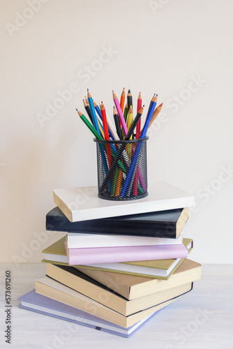 Pencil holder with colored pencils and stack of books on rustic table. Copy space