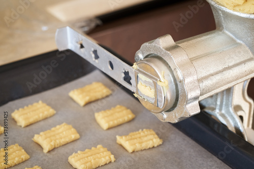 Pressing pastry dough through a mincer to prepare Christmas cookies