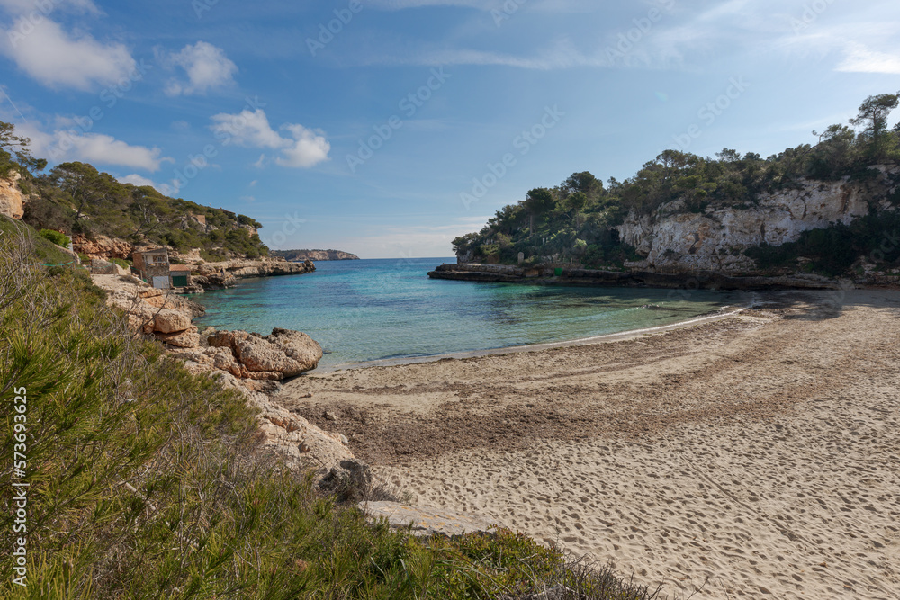 Mallorca beach. General view of Cala Llombards beach, with remains of Posidonia Oceanica on the sand. A cove with crystal clear turquoise water, with small houses with jetties for small fishing boats.