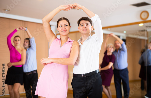 Cheerful young guy and girl practicing ballroom dances in ballroom