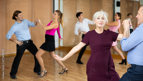 elderly couple is engaged in Latin dance studio and learns movements of cha-cha-cha dance