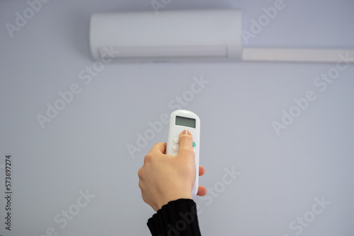 Split air conditioner on a white wall. A woman's hand switches the mode. Summer heat.