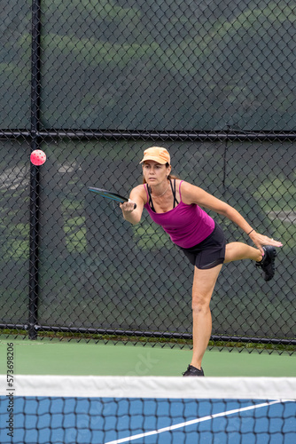 A female player hits a pickleball serve.