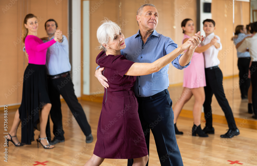 Positive active elderly couple enjoying slow foxtrot in dance studio. Amateur social dancing concept