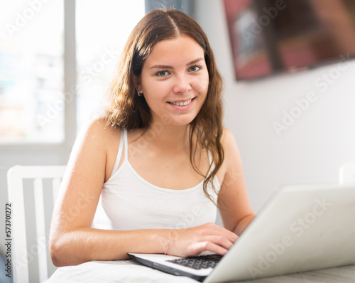Portrait of positive young woman working on laptop sitting at table in living room Free Download Portrait of positive young woman working on laptop sitting at table in living room - GFXLoad