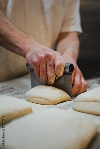 Close up view of baker cutting bread dough with steel scraper in bakery photo