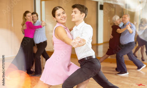 Cheerful attractive young girl learning to dance waltz with guy partner in dancing class..