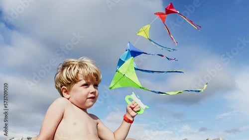 View from behind of cute blond boy holding many kites