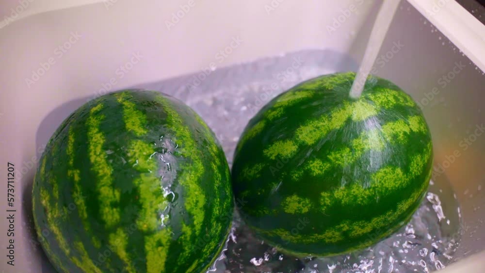 Striped round watermelons in white sink under the water flow, top view